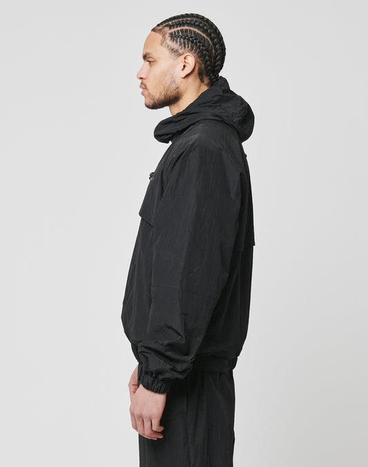A man with braided hair stands in profile against a plain background, wearing the LIVE FAST DIE YOUNG Live Fast Nylon Jacket with seitliche Eingrifftaschen and matching oversized pants.