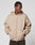 Wearing the LFDY Double Hooded Zip by LIVE FAST DIE YOUNG, a person stands with hands in pockets, looking down to the side. The beige zip-up has small LIVE FAST text on the chest, waffle lining, and is set against a plain light gray background.