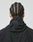 A person with neat cornrows is shown from behind, wearing the LIVE FAST DIE YOUNG Live Fast Nylon Jacket in black with textured fabric and side pockets, hood down, against a plain light background.