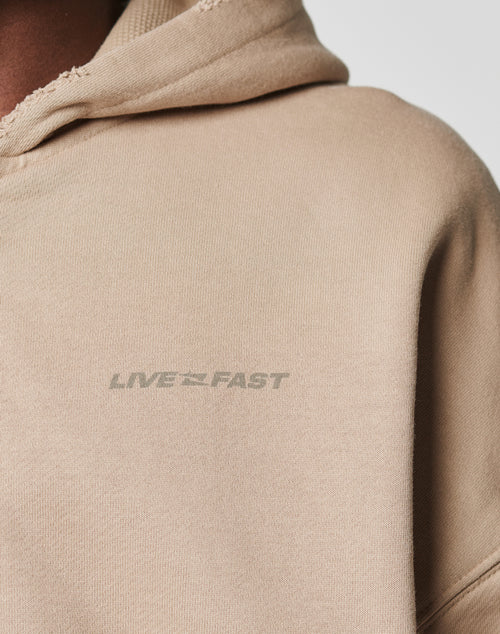 Close-up of the beige LFDY Double Hooded Zip by LIVE FAST DIE YOUNG, featuring light gray LIVE FAST print on the chest, subtle distress effect, and a partial double hood for a relaxed look.