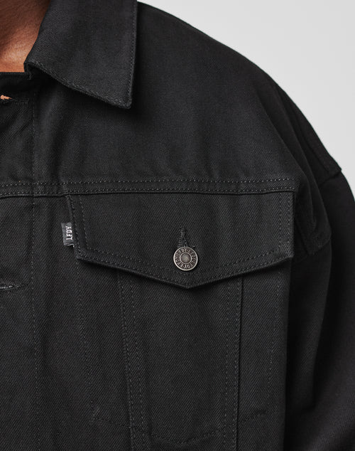 Close-up of the upper part of the LFDY Denim Jacket by LIVE FAST DIE YOUNG, made from 100% cotton with a metal button, small fabric tag on the chest pocket, pointed collar, and visible stitching.