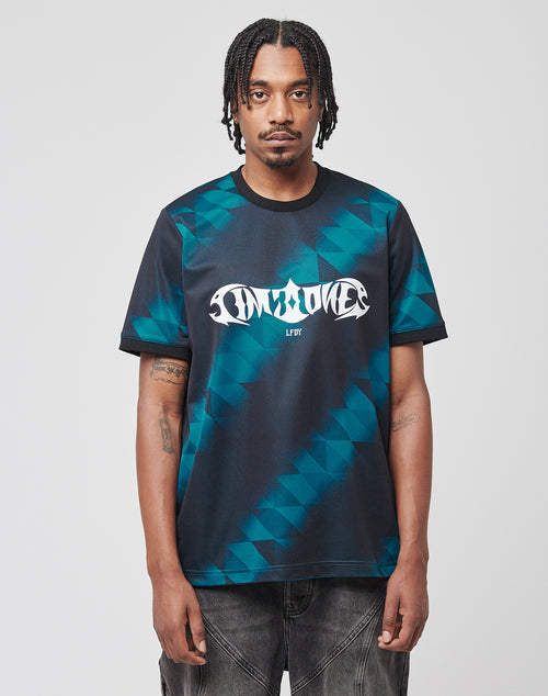 A man with braided hair wears the LIVE FAST DIE YOUNG Live Fast Jersey Tee, a dark Regular Fit polyester shirt with geometric patterns and bold white graphic text on the chest. He stands facing forward against a plain light background.