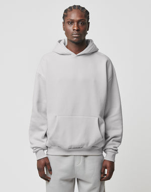 A person with braided hair faces forward, wearing the LIVE FAST DIE YOUNG Basic Blank Hooded in light gray and matching sweatpants made from soft Baumwolle and polyester, set against a plain, light background.