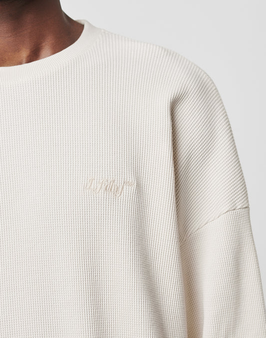 Close-up of a person wearing the cream-colored Basic Waffle Longsleeve by LIVE FAST DIE YOUNG, featuring an oversize fit and subtle chest logo embroidery. Image shows neck, shoulder, and upper chest against a plain background.