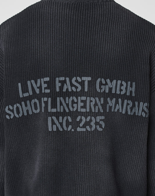 A close-up of the backprint on the black LFDY Washed Knit Sweater by LIVE FAST DIE YOUNG, featuring faded gray text and crafted from 100% Baumwolle for all-day comfort and style.