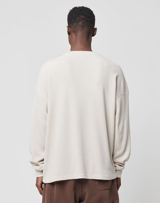 A person stands facing away from the camera, wearing the LIVE FAST DIE YOUNG Basic Waffle Longsleeve in light beige with a subtle logo-stitch and brown pants, set against a plain light background.