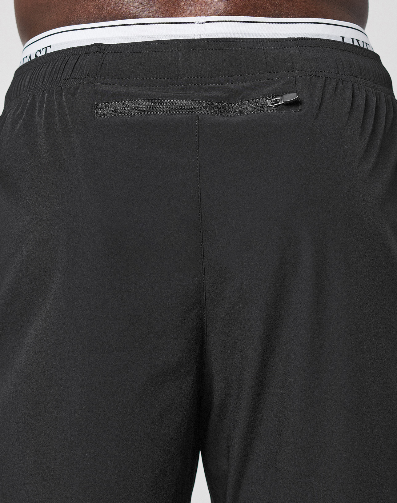 Close-up of the back of a person wearing LFDY Performance Pants by LIVE FAST DIE YOUNG, featuring a zippered pocket below the waistband, LFDY branding, and a visible white elastic waistband above.