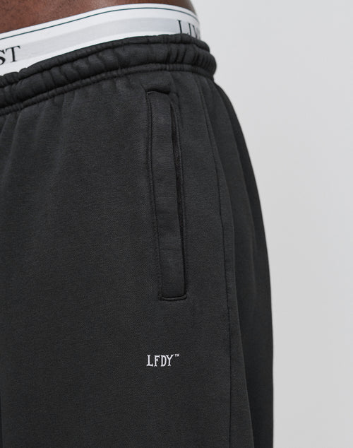 Close-up of a person wearing the LIVE FAST DIE YOUNG Basic Wide Jogger, featuring an oversized fit, white embroidered LFDY logo near the pocket, and a white elastic waistband with black lettering.