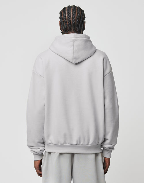 A person with braided hair faces away from the camera, wearing the LIVE FAST DIE YOUNG Basic Blank Hooded in light gray and matching shorts, both in a soft polyester-baumwolle blend, set against a plain white background.