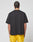 A person with braided hair faces away, wearing the LIVE FAST DIE YOUNG LFDY Bark Tee in black vintage wash and bright yellow oversized shorts, set against a plain white background.