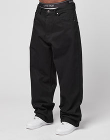 Someone wears LFDY Baggy Denim—baggy, loose-fitting black jeans made from 100% Baumwolle—with white sneakers and black LIVE FAST underwear visible at the waistband. The plain, light background highlights the outfit.