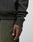 A close-up of a hand resting by the side, wearing the LIVE FAST DIE YOUNG LFDY Supply Hooded in an oversized fit with green textured Baumwolle Polyester pants, set against a plain light background.