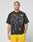 A man with braided hair wears the LIVE FAST DIE YOUNG LFDY Bark Tee, a black, vintage wash shirt with large dog graphics and yellow LIVE FAST text. He pairs it with bright yellow athletic shorts against a plain gray background.