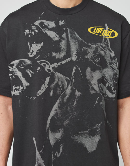 Someone wears the LFDY Bark Tee by LIVE FAST DIE YOUNG, a black vintage-wash oversize t-shirt with three snarling black dogs and a yellow oval LIVE FAST logo.