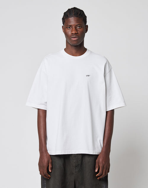 A man faces forward against a plain background, wearing the LIVE FAST DIE YOUNG LFDY Monaco Boys Tee in Oversize Fit with short sleeves and small chest text. Made from 100% Baumwolle, he pairs it with dark pants.