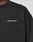 Close-up of a person wearing the LIVE FAST DIE YOUNG Basic +49 Chest Sweater in black, featuring a white "+49" chest print. Only part of the neck, shoulder, and upper chest is visible.