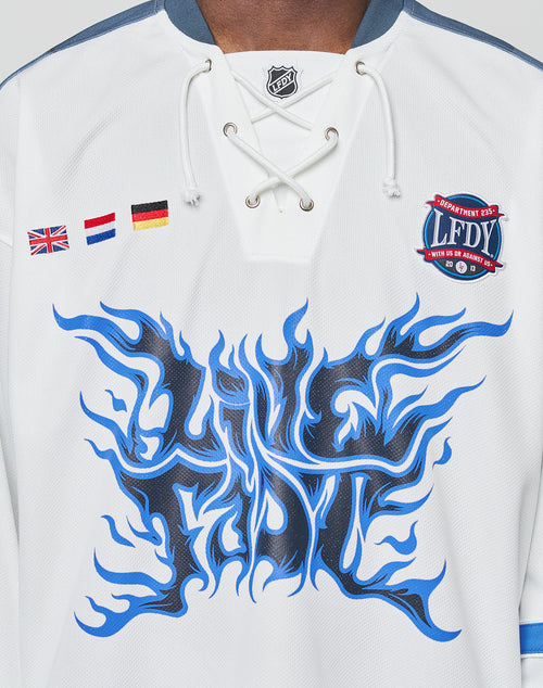 The LFDY Flames Jersey by LIVE FAST DIE YOUNG is an oversized white polyester hockey jersey with blue flame graphics, a stylized LFDY front print, UK/Netherlands/Germany flag patches, and a round LFDY badge on the right chest.