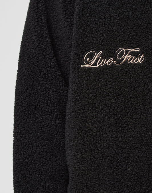 Close-up of the LFDY Teddy Jacket by LIVE FAST DIE YOUNG, featuring black textured fleece, raglan sleeves, and "Live Fast" embroidered in cursive with light-colored thread.