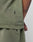 A close-up shows a person in the LIVE FAST DIE YOUNG Basic +49 Tee, Oversize Fit in olive green. Visible are the side seam, small black tag, part of a tattooed arm, and subtle topstitching at the neckline.