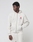 A young man wears a light beige LFDY Heavyweight Lounge Zip Hooded by LIVE FAST DIE YOUNG with matching sweatpants. The 100% cotton hoodie has a red and black LIVEFAST logo on the chest. He stands against a white background, looking to the side.