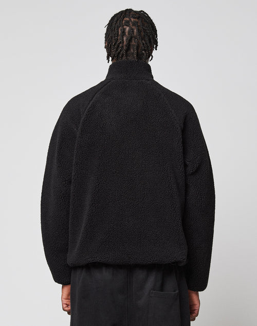 A person with short, twisted hair is seen from behind wearing a black LFDY Teddy Jacket by LIVE FAST DIE YOUNG and black pants, standing against a plain light gray background.