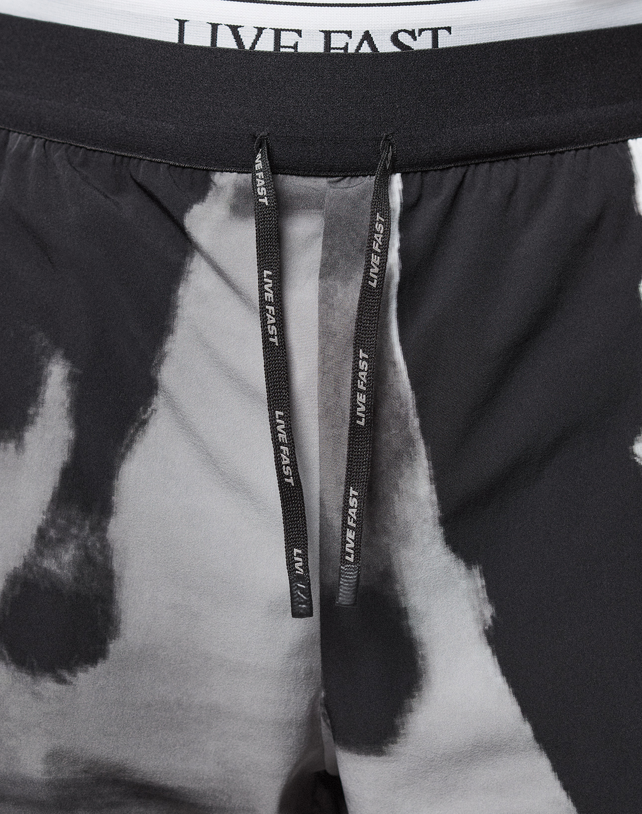 Close-up of LFDY Performance Shorts by LIVE FAST DIE YOUNG in black and white tie-dye, featuring a reflective LIVE FAST logo on the black drawstrings, a white waistband with black LIVE FAST text, regular fit, and lightweight fabric for comfort.