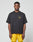 A man faces forward against a plain light gray background, wearing the LIVE FAST DIE YOUNG LFDY Circle Dog Tee in loose oversize fit with a small yellow graphic, paired with yellow shorts.