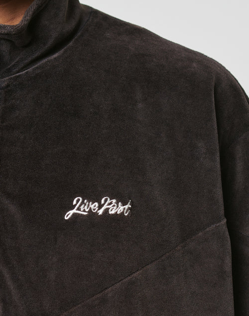 Close-up of the LFDY Velour Jacket by LIVE FAST DIE YOUNG, featuring a dark brown velour fabric, Stehkragen, relaxed oversize fit, and white Live Fast logo stitched on the chest. The soft texture is clearly visible.