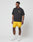A man wears the LIVE FAST DIE YOUNG LFDY Circle Dog Tee, black and loose with a small yellow logo, paired with yellow shorts, white socks, and white sneakers as he stands against a plain white background looking to his left.
