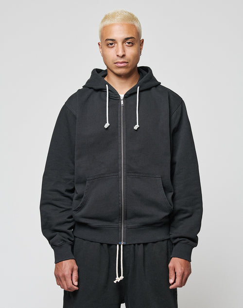 A person with short blond hair wears a black LIVE FAST DIE YOUNG LFDY Lightweight Hooded Zip and matching black pants, standing facing the camera against a plain light background.