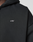 Close-up of the Basic Evidence Hooded Zip by LIVE FAST DIE YOUNG, a black oversized hoodie with bold white branding on the chest. Only part of the wearer’s neck and shoulder shows against a plain light background.