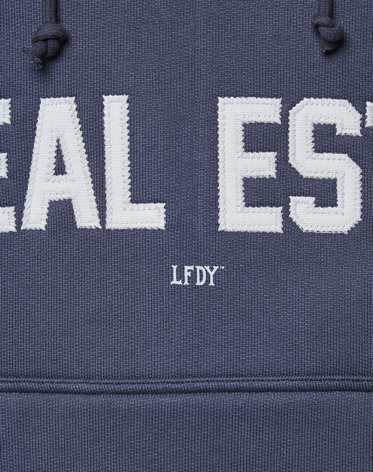 Close-up of the LFDY Heavyweight Lounge Hooded by LIVE FAST DIE YOUNG: a blue, Regular Fit hoodie made from 100% Baumwolle, featuring large white “EAL EST” embroidery, smaller LFDY text below, and visible drawstrings for added style.