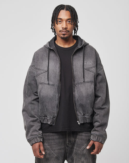 A man with medium-length braids wears a black t-shirt, LIVE FAST DIE YOUNG Tribal Denim Hooded Zip jacket, and matching gray jeans, standing against a plain light background.