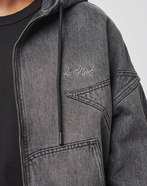 Close-up of a person wearing the LIVE FAST DIE YOUNG Tribal Denim Hooded Zip: a grey jacket with Tribal Panels, visible stitching, chest Live Fast embroidery, hood, zipper, and eye-catching Logo-Stick detail.