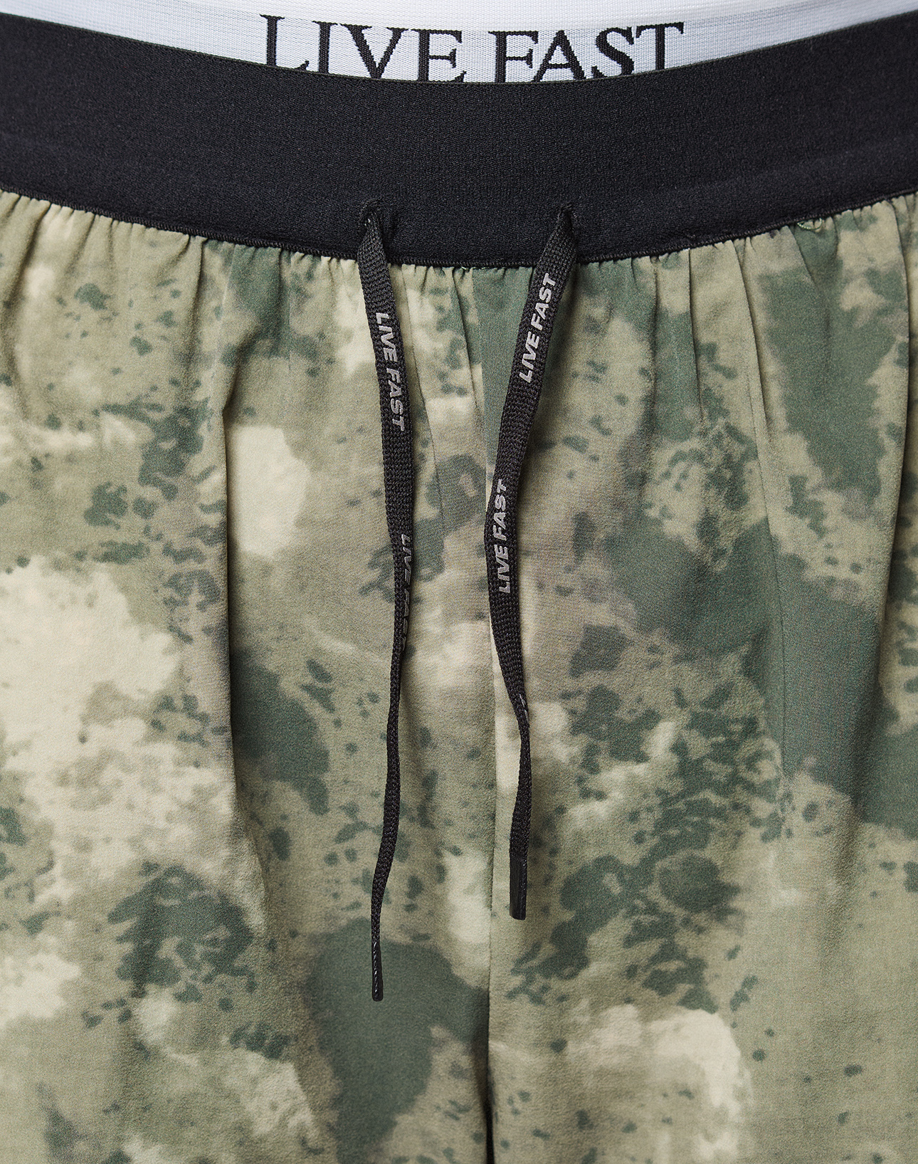 Close-up of the waistband and drawstrings of LFDY Performance Running Shorts by LIVE FAST DIE YOUNG. The black elastic waistband has a reflective LIVE FAST logo print in white, matching drawstrings, and offers a comfortable regular fit.