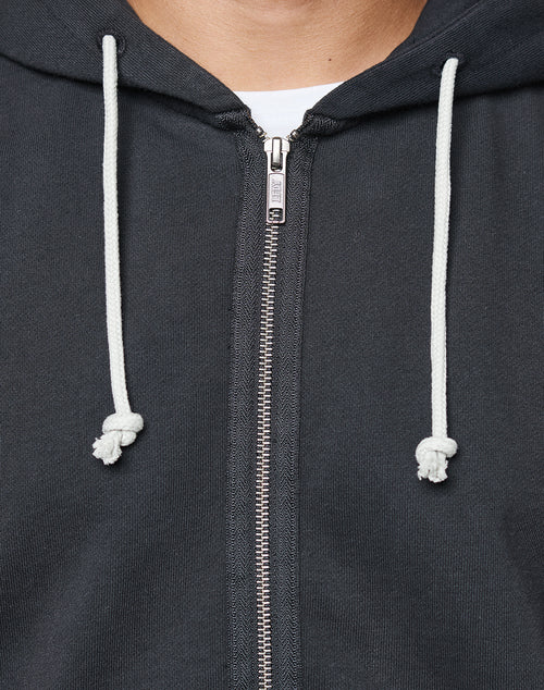 Close-up of a person wearing the LIVE FAST DIE YOUNG LFDY Lightweight Hooded Zip. Features include white knotted drawstrings, a partially zipped front revealing a white shirt, and 100% Baumwolle fabric for comfort.
