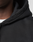 Close-up of a person wearing the LIVE FAST DIE YOUNG Basic Evidence Hooded Zip in black over a white shirt; only part of the face, neck, and shoulder are shown, highlighting the fabric, seam details, and subtle brand logo on the hoodie.