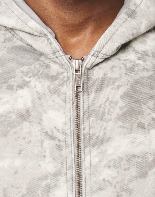 Close-up of a person wearing the Live Fast Canvas Jacket by LIVE FAST DIE YOUNG, featuring a light gray, textured marbled pattern, metal zipper pulled up most of the way, and an oversize fit showing the upper chest and neck.