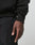 A close-up of a right hand and wrist wearing the oversized fit Live Fast Garment Hooded by LIVE FAST DIE YOUNG and textured black pants, set against a plain light background.