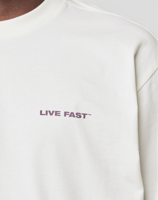 A close-up of the LFDY Grand Theft Tee by LIVE FAST DIE YOUNG, a white 100% Baumwolle crewneck with "LIVE FAST™" in small bold purple letters on the left chest.