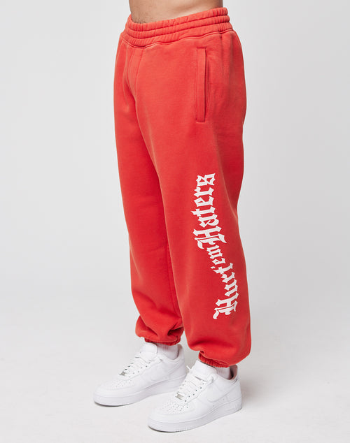 A person wears LIVE FAST DIE YOUNG LFDY Haters Jogger—bright red, wide fit sweatpants with bold Butter Haters text and elastic waistband—paired with white Nike sneakers against a plain light gray background.