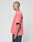 A person with a shaved head in profile wears the LIVE FAST DIE YOUNG Basic Evidence Tee—an oversize, faded pink shirt with a Flag-Label and black and white back text—paired with dark pants against a plain light background.