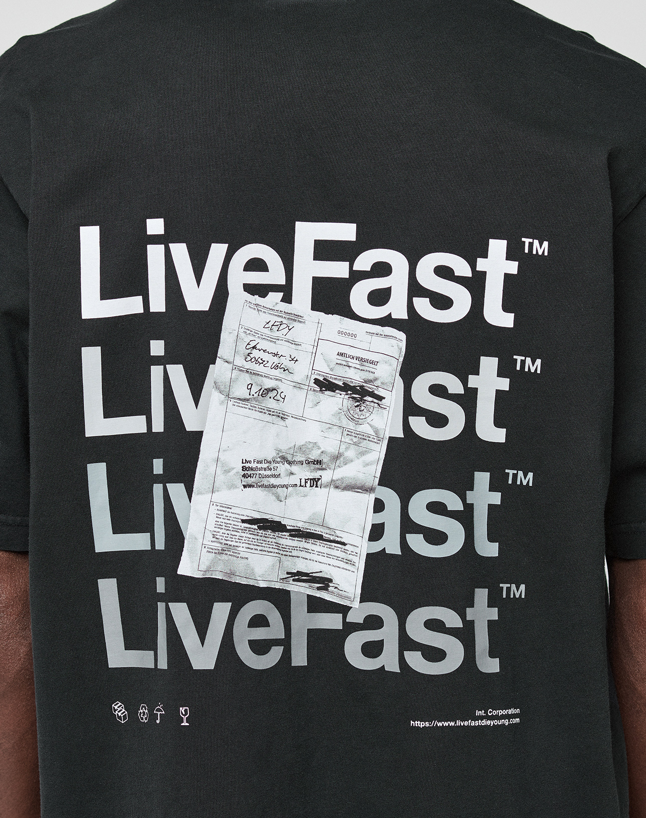 Back of the black Basic Evidence Tee by LIVE FAST DIE YOUNG with "LiveFast" four times in bold white, a crumpled receipt image over the text, small symbols, 100% Baumwolle, front/back print, and website link at the bottom.