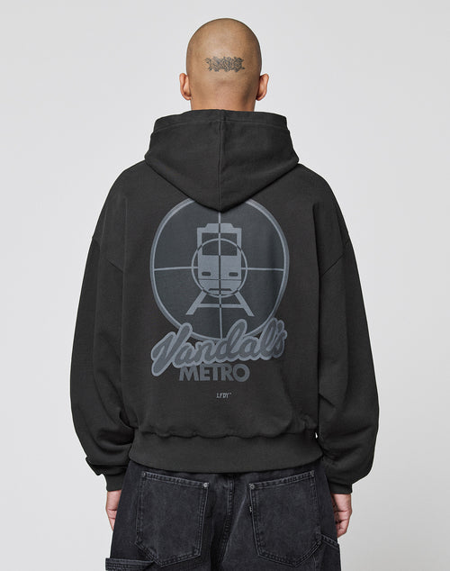 A person with a shaved head and neck tattoo, facing away, wears the LFDY Vandals Hooded by LIVE FAST DIE YOUNG—an oversized black 100% cotton hoodie featuring a subway train in crosshairs and "Vandals METRO" on the back.