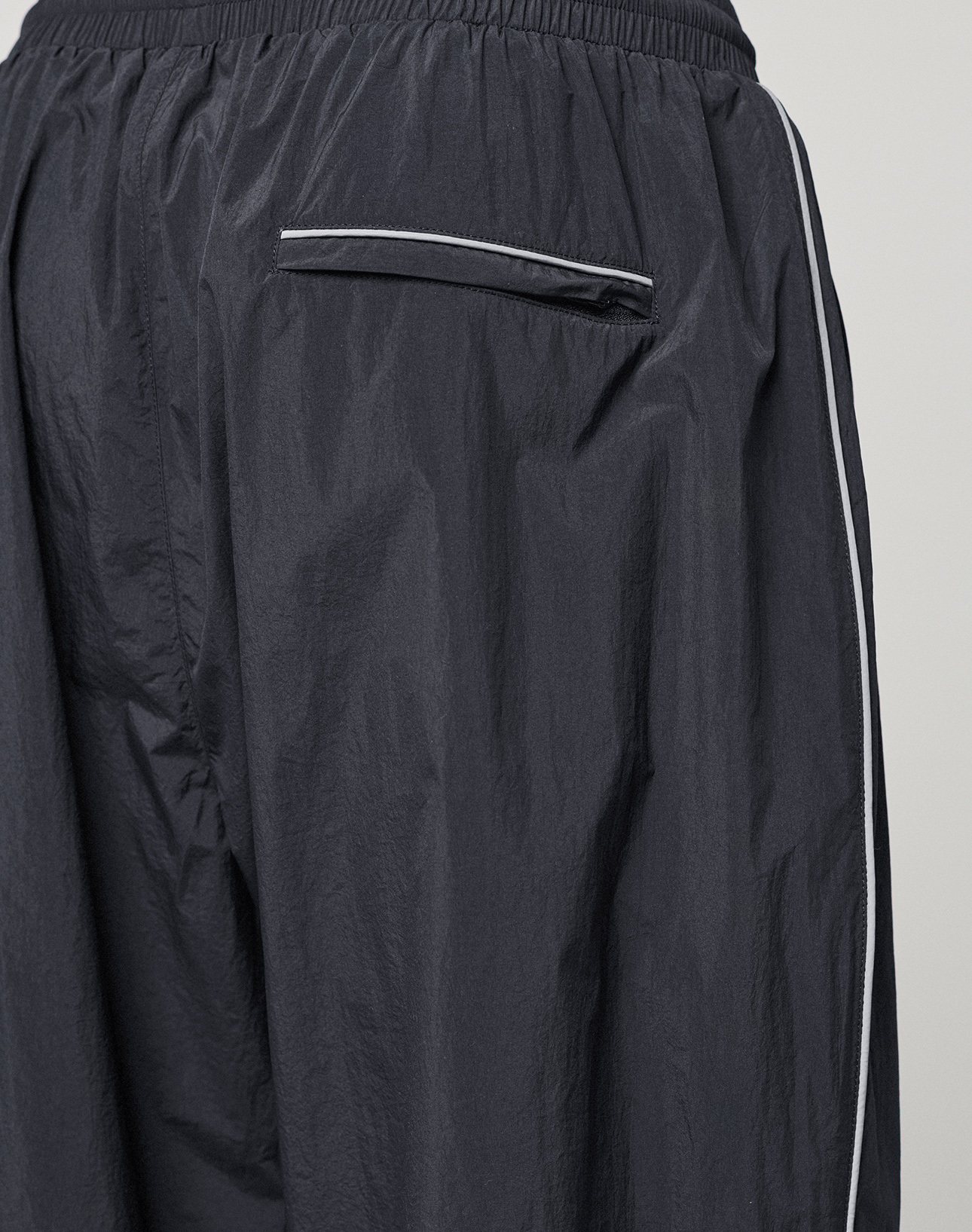 Close-up of the back of LFDY Performance Trackpants by LIVE FAST DIE YOUNG in dark navy, oversize fit, with a white-trimmed pocket, white side stripe, elastic waistband, and slight sheen. Made from 100% nylon.