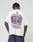 A person wearing the LFDY Grand Theft Tee by LIVE FAST DIE YOUNG—an oversize white 100% cotton shirt with bold front and back prints. The back displays "INTERNATIONAL BRANCH NETWORK," "LIVEFAST," several countries, and a vintage race photo in purple.