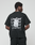 A person faces away from the camera wearing the LIVE FAST DIE YOUNG Basic Evidence Tee, an oversized black T-shirt with “LiveFast” repeatedly printed in white on the back and a visible white tag attached.