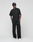 A person poses against a plain background wearing the oversized black 'Basic Evidence Tee' by LIVE FAST DIE YOUNG, paired with black pants, white sneakers, and a black baseball cap. Hands in pockets, they gaze to the side.