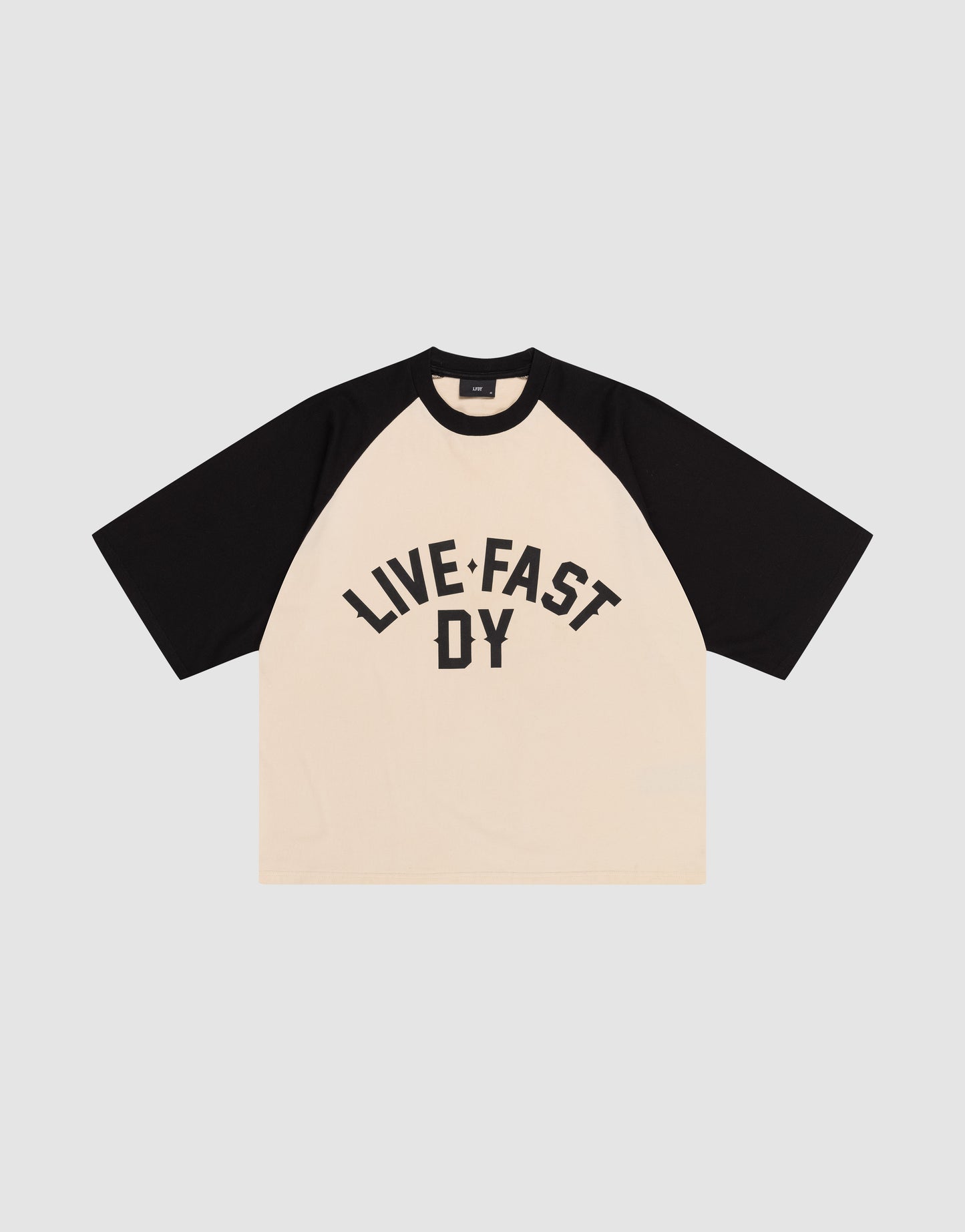 The Live Fast Raglan Tee by LIVE FAST DIE YOUNG features a cream body, black raglan sleeves, boxy oversized fit, and bold "LIVE FAST DY" text on the front. Made from 100% cotton.