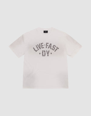 The Live Fast Rivet Tee by LIVE FAST DIE YOUNG is a white short-sleeve t-shirt featuring "LIVE FAST DIE YOUNG" in bold, patterned letters across the chest and subtle distressing for a worn-in edge. Displayed flat on a light background. | plain